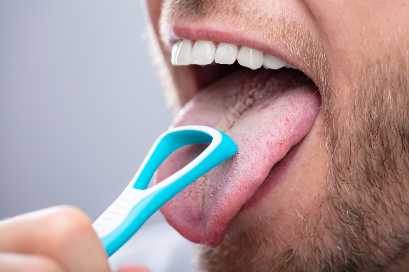 Person cleaning tongue with scraper to improve oral hygiene in Arlington Heights, IL